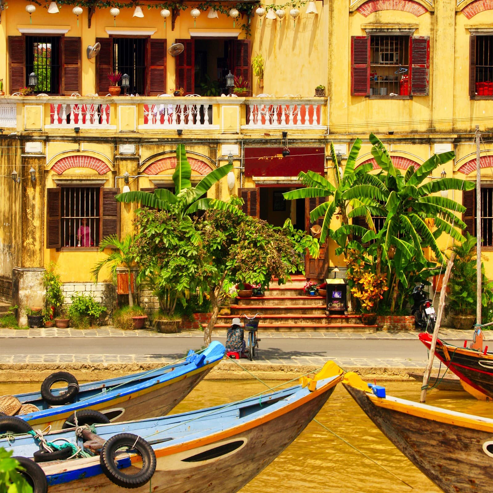 Вид с моста Ан Хой на вечерний Хойан — гирлянды, фонари и отражения на реке Тхубон, лодки у набережных и живая ночная часть острова Ан Хой рядом.