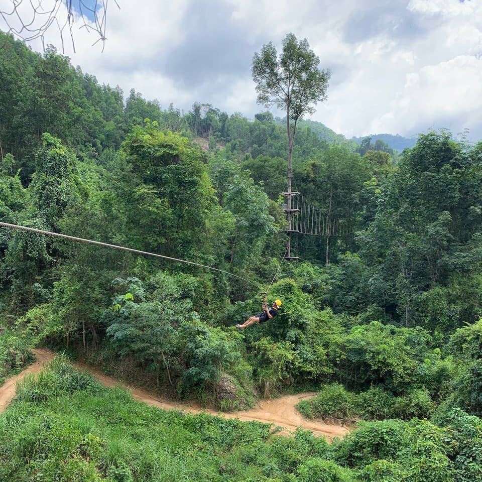Турист летит по зиплайну над тропическими деревьями, где линии маршрута прорезают зелёную глубину Kong Forest